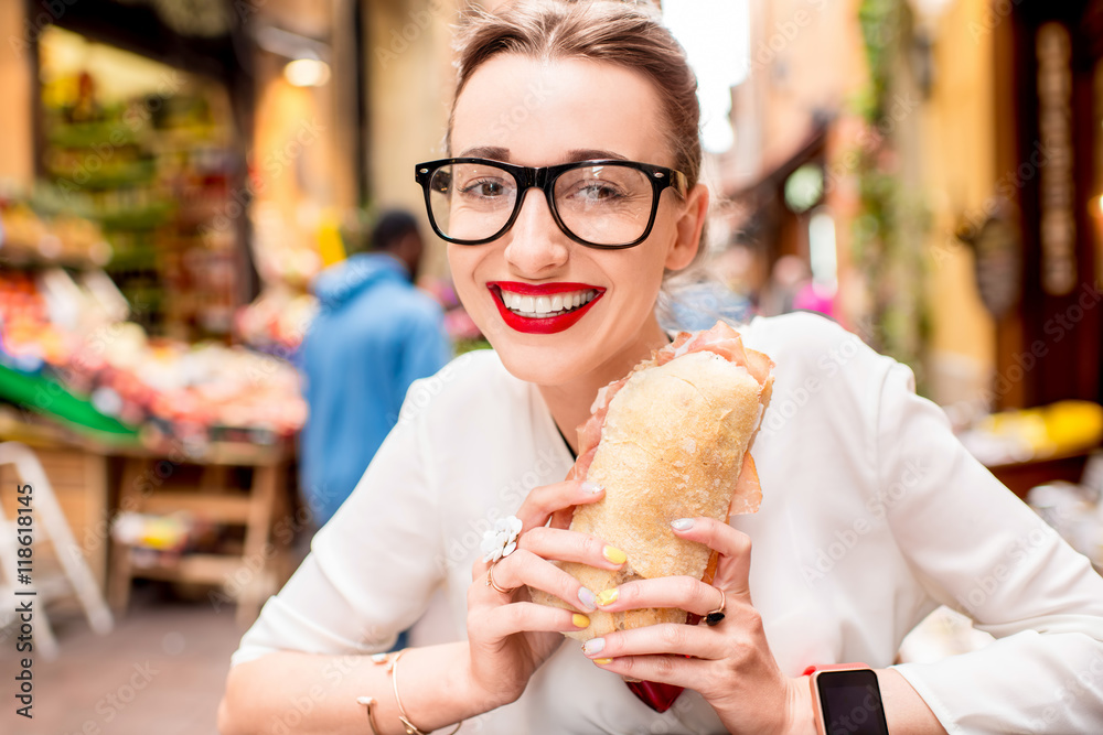 在博洛尼亚街头的户外咖啡馆里，一位年轻女子拿着火腿帕尼尼三明治坐着