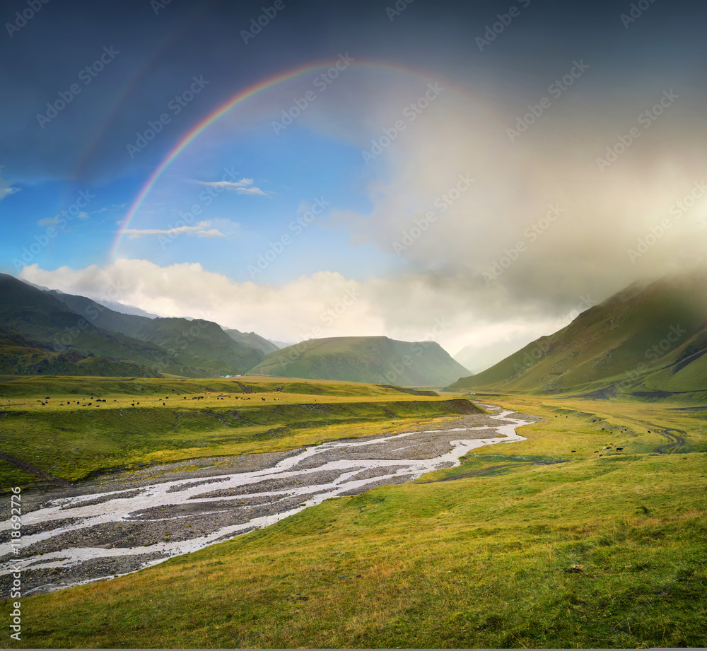 Rainbow in the mountain valley during rain. Beautiful natural landscape in the summer time