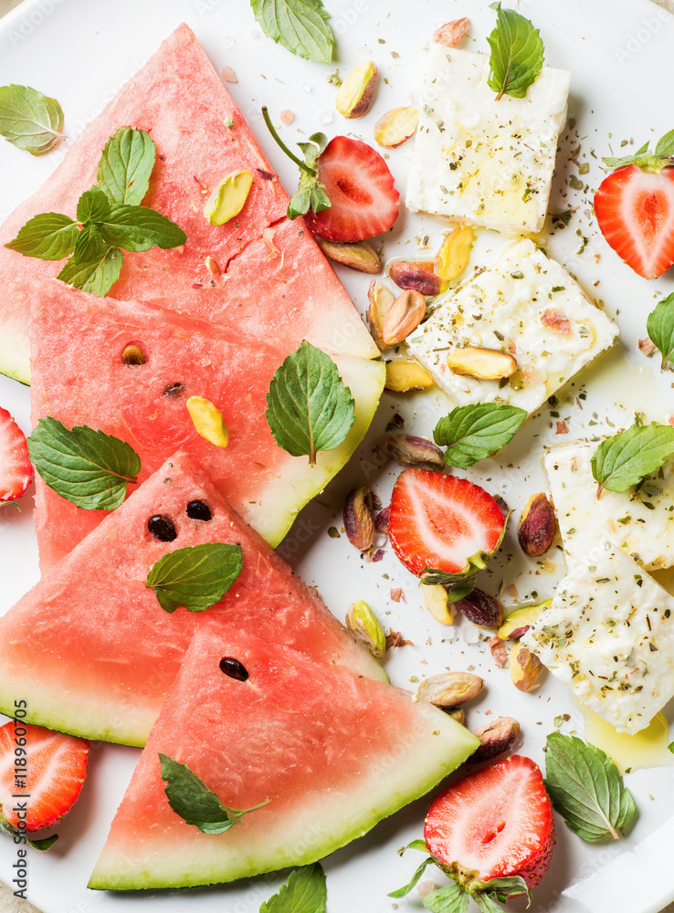 夏季西瓜、草莓和羊乳酪沙拉，白盘子里有冬叶和开心果。