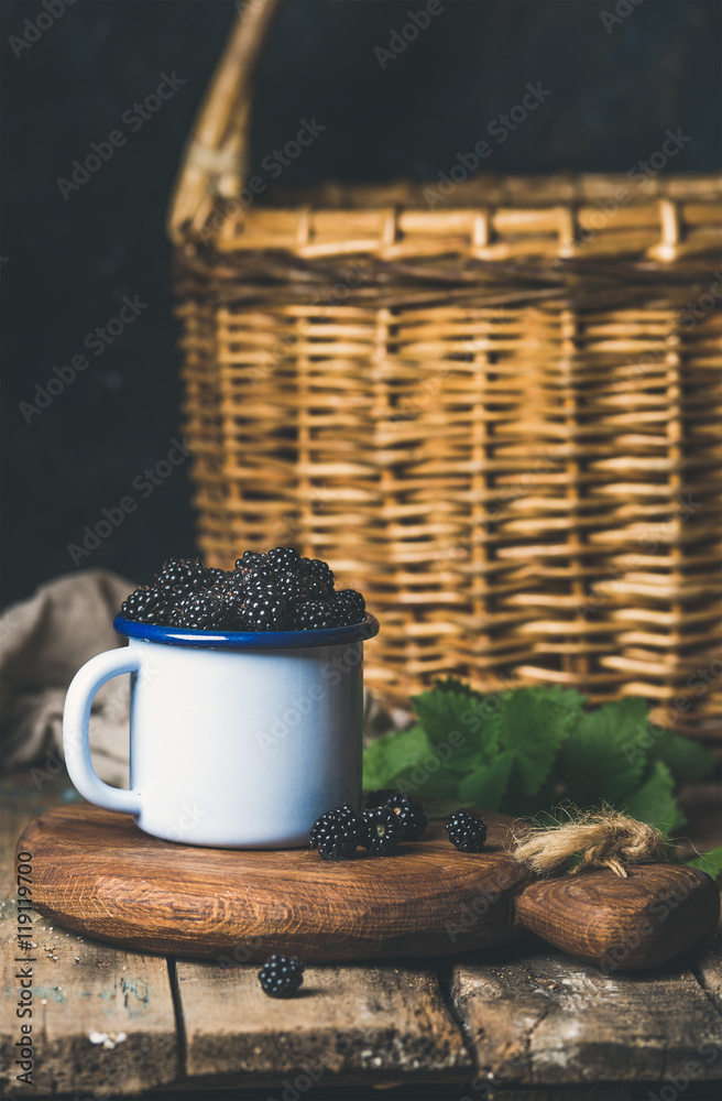 新鲜黑莓装在白色杯子里，放在乡村餐桌上的圆形木板上，后面是桦树皮