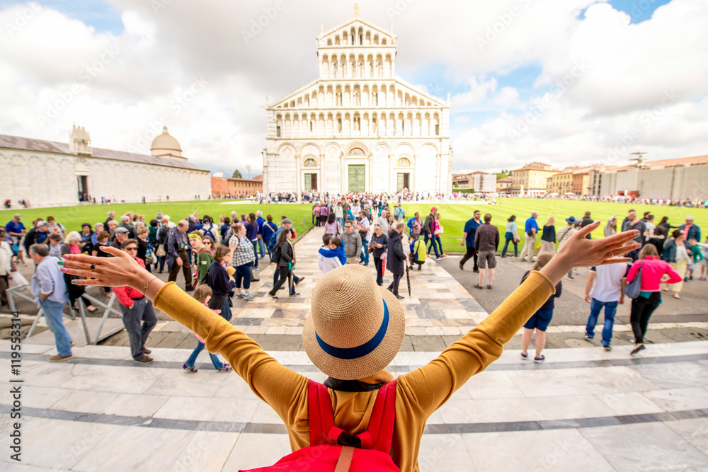 Young female traveler rasing hands enjoying great cathedral in Pisa old town in Italy