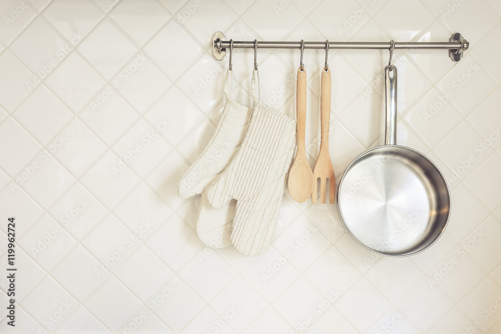 瓷砖墙上带木勺叉的厨房用具手套和平底锅