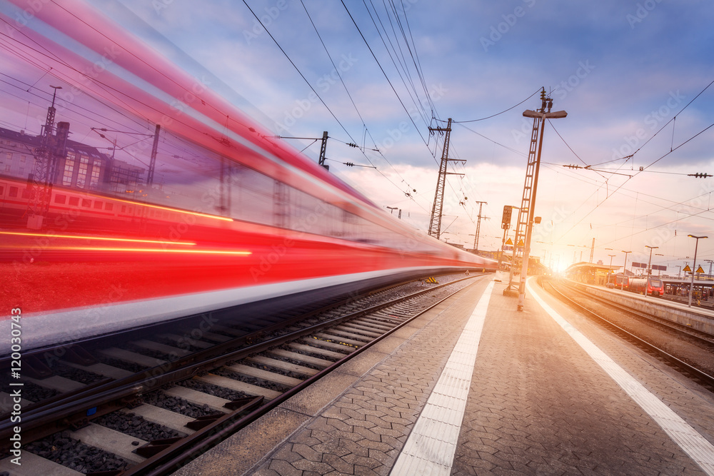 High speed red passenger train on railroad track in motion at beautiful sunset. Blurred commuter tra