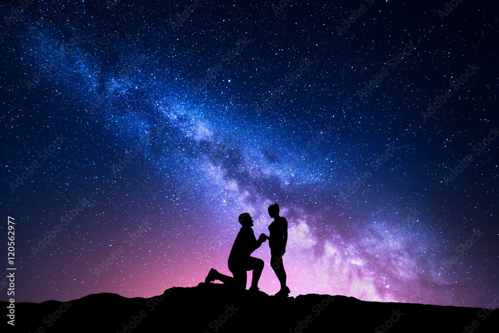 Milky Way. Night landscape with silhouettes of a man making marriage proposal to his girlfriend and 