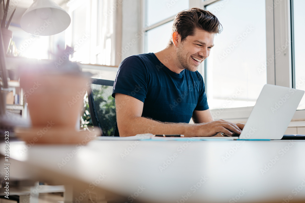 快乐的年轻商人在办公桌上使用笔记本电脑