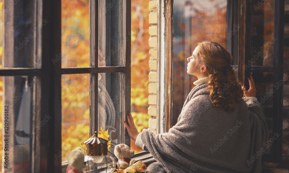 快乐的年轻女子在敞开的窗户前享受秋天的新鲜空气