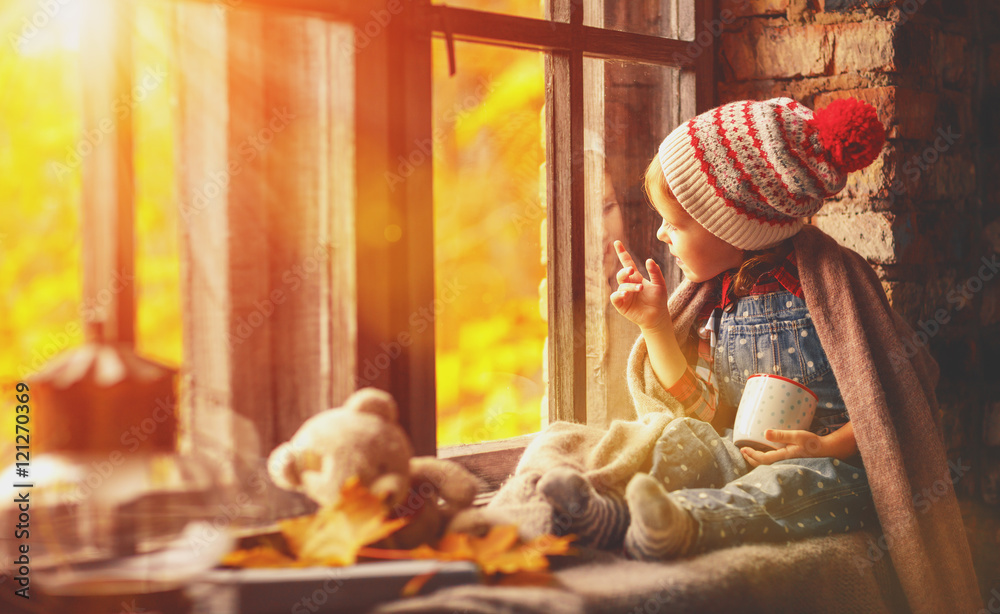 拿着杯茶的小女孩透过窗户看秋天的大自然