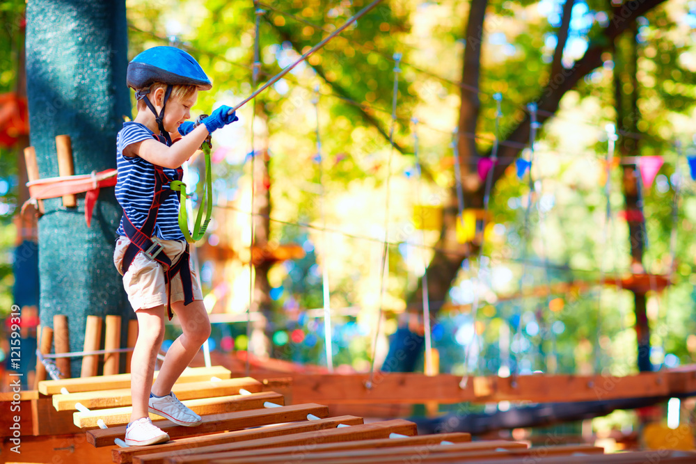 小男孩在树林中穿过电缆路线，在冒险公园进行极限运动