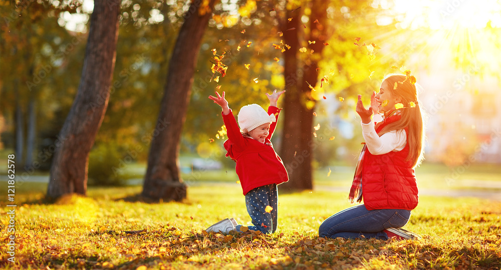 幸福的家庭母亲和小女孩玩耍并扔树叶