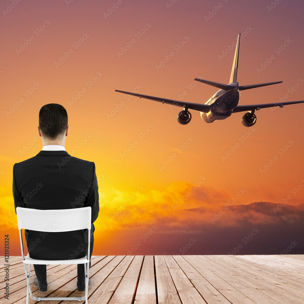 Businessman looking at sunset and airplane