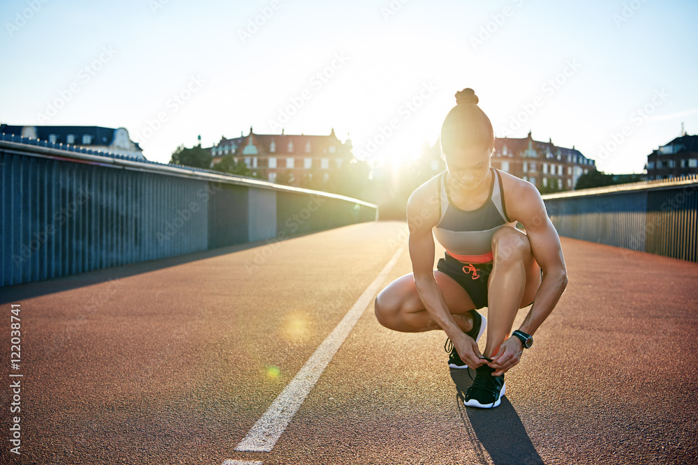 肌肉发达的女人把跑鞋系在桥上