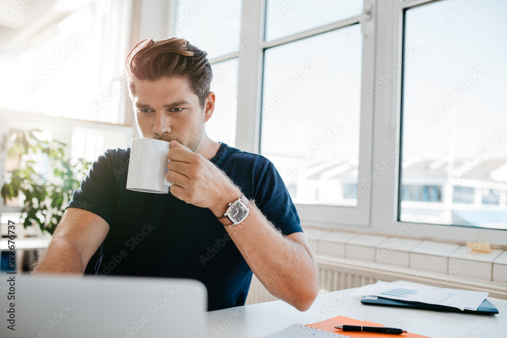 Businessman drinking coffee and working on laptop at office