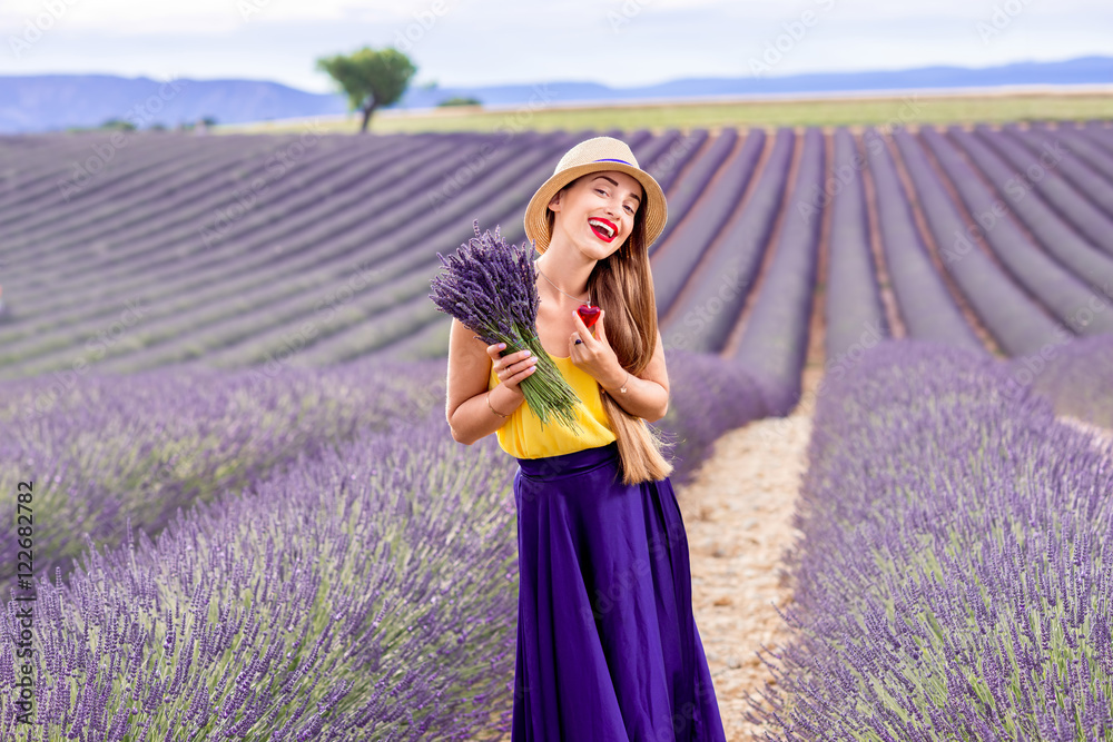 年轻漂亮的女人穿着紫色长裙，拿着薰衣草花束站在薰衣草地上