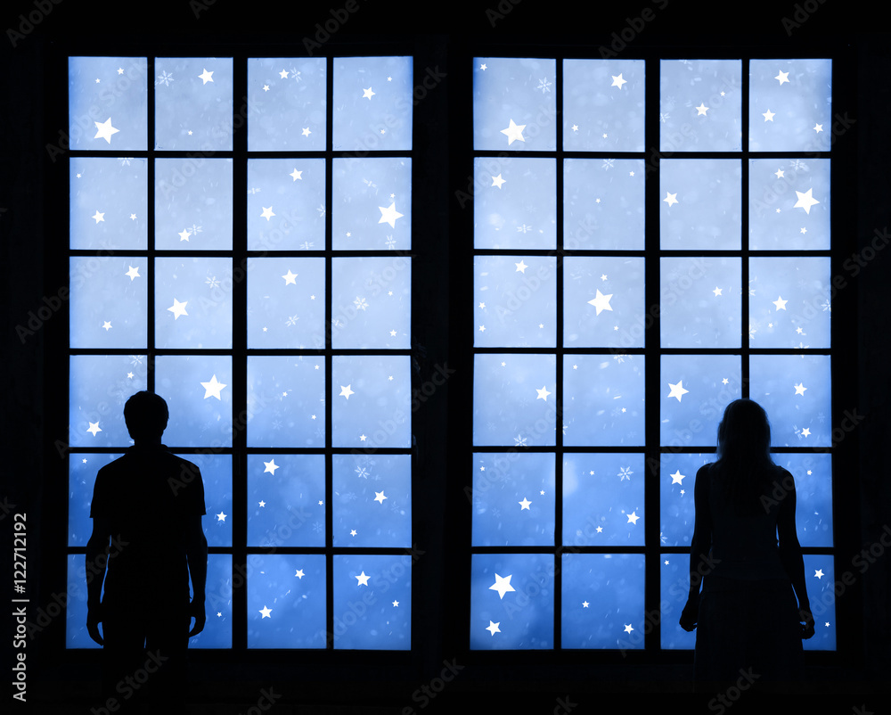一对夫妇站在大窗户里看着蓝色的冬季度假明星的剪影