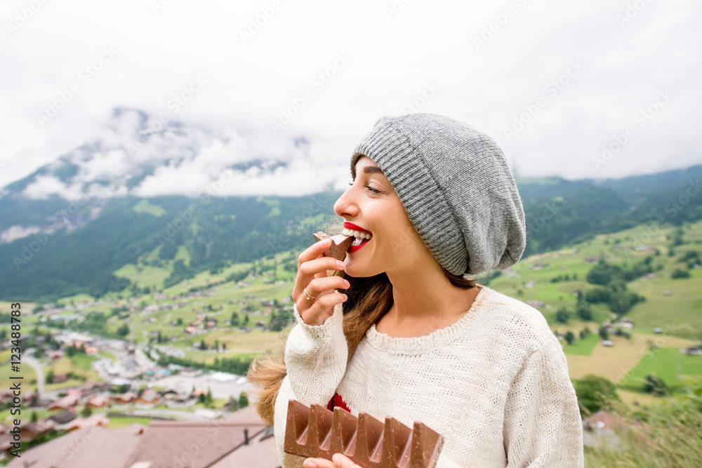 Young woman eating chocolate outdoors in the mountains. Having great vacations in Switzerland