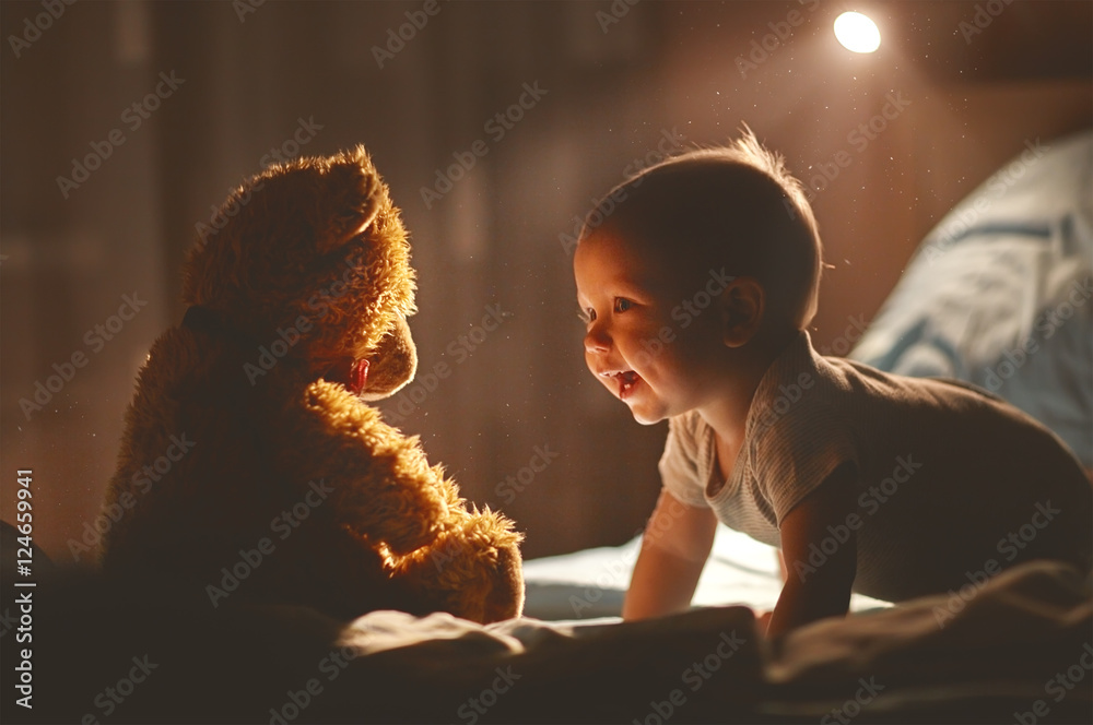 快乐的宝宝在床上和泰迪熊一起大笑