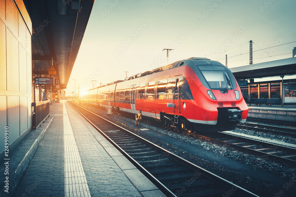 Beautiful railway station with modern high speed red commuter train at colorful sunset. Railroad wit