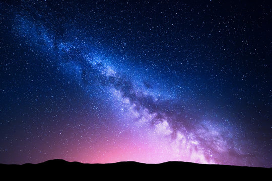 银河和山上的粉红色光芒。夜晚五彩缤纷的风景。夏天的星空和山丘。Be