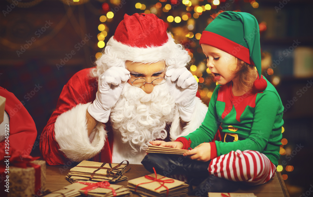 Santa Claus and a elf child in a Christmas working, reading lett