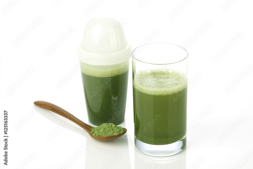杯子里的绿色蔬菜汁和勺子上的蔬菜粉末的特写
