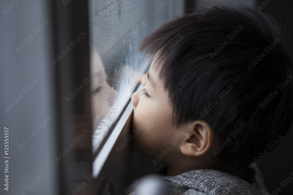 3歳の男の子は一人で窓の外を見ている3-year-old boy is looking out of the window alone