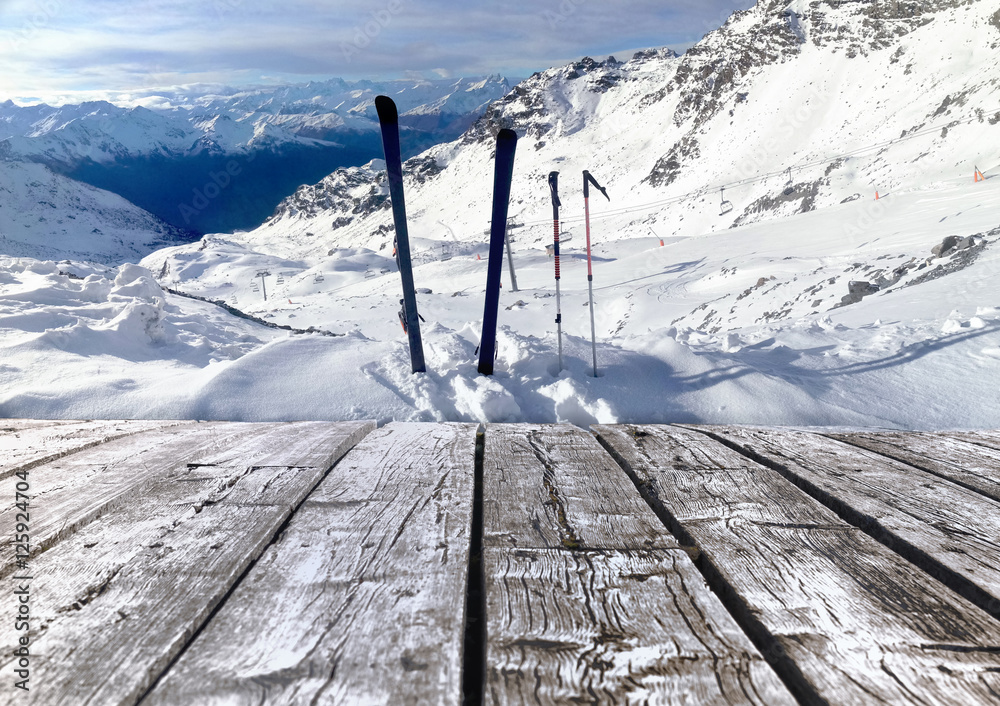skis plantés dans la neige devant terrasse en bois