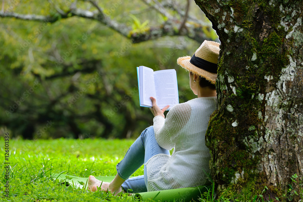 一位中年妇女坐在公园的树下看书