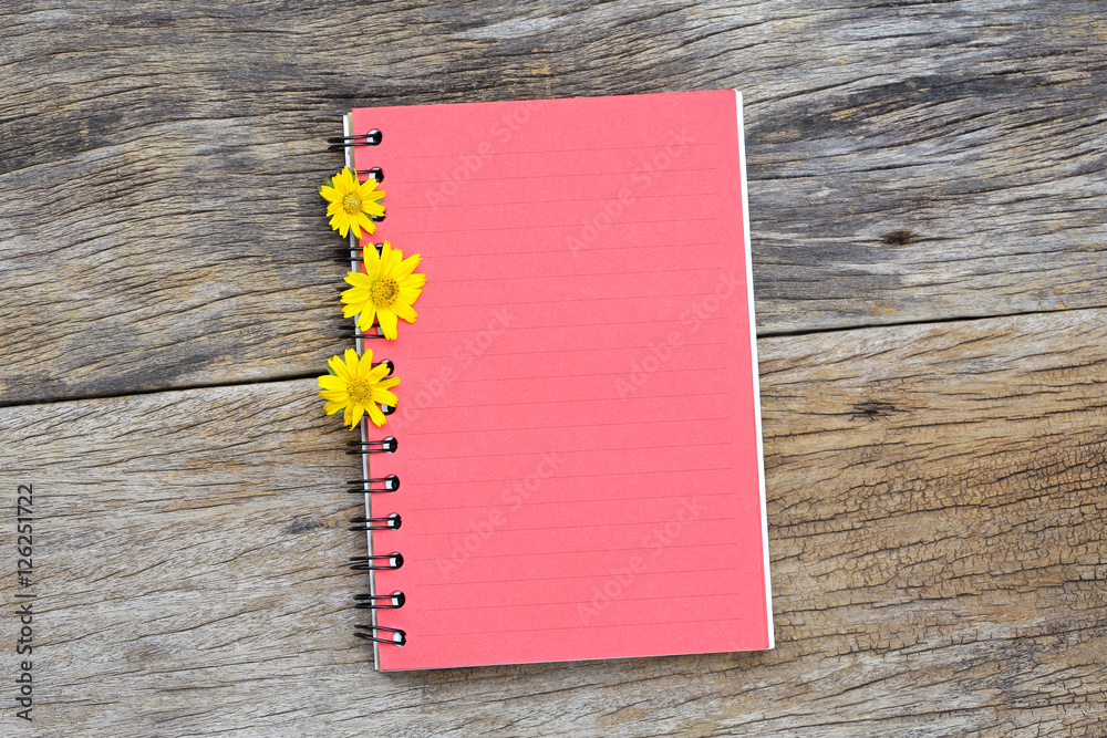 木桌上有黄色花朵的红色笔记本