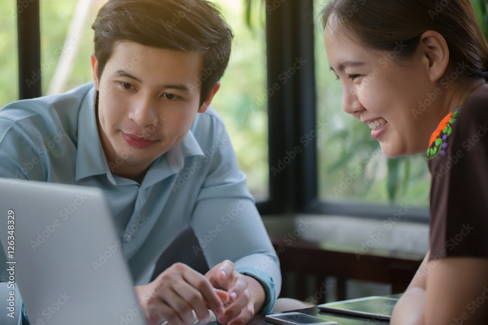 年轻的亚洲商人和女人在咖啡馆会面，用笔记本电脑做演示