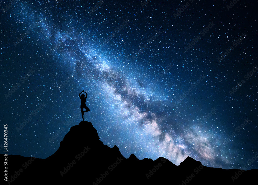 银河系，一个站着的女人在山顶练习瑜伽的剪影。风景