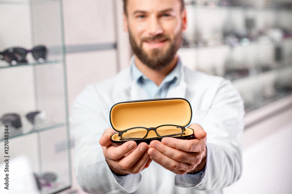 英俊的眼科医生拿着眼镜进行试用。验光师主动提出要戴一副眼镜
