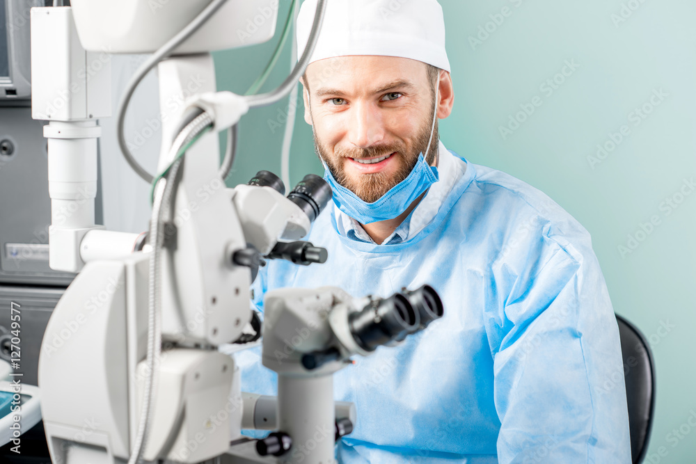 手术室里戴着显微镜、身穿制服、面带微笑的眼科医生画像