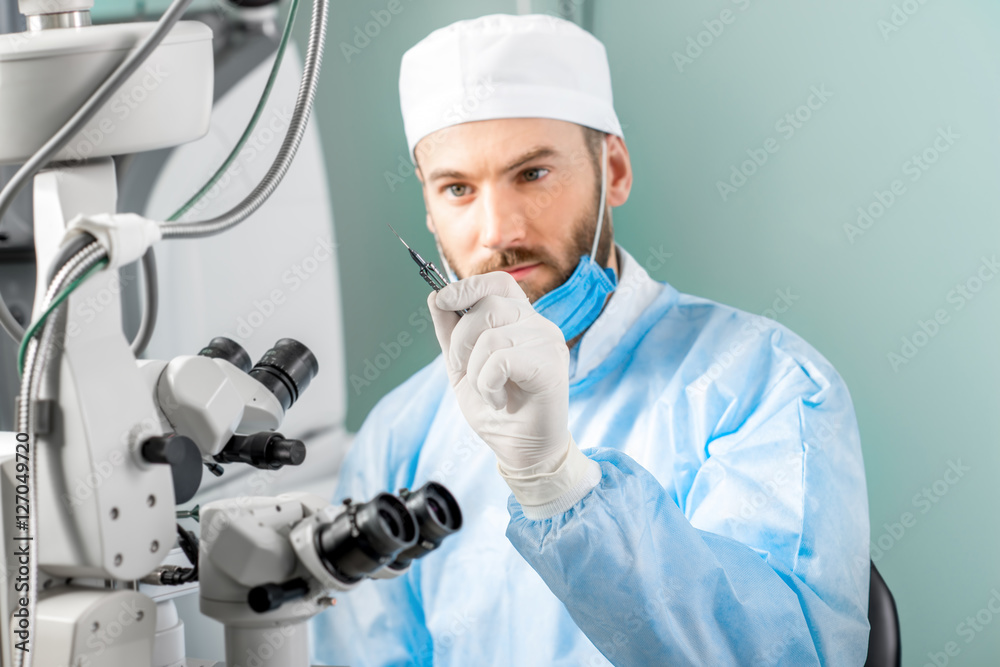 眼科医生拿着小手术剪刀在手术室靠近显微镜的地方进行眼部手术