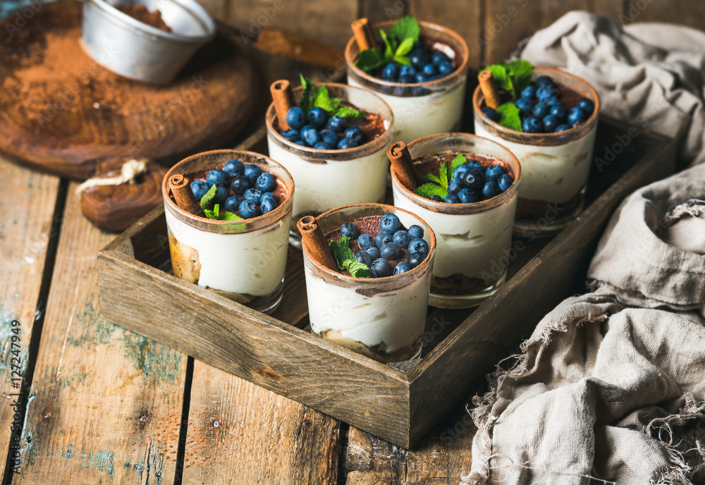 自制提拉米苏甜点，装在玻璃杯里，配肉桂、薄荷和新鲜蓝莓，装在木托盘里，放在rus上