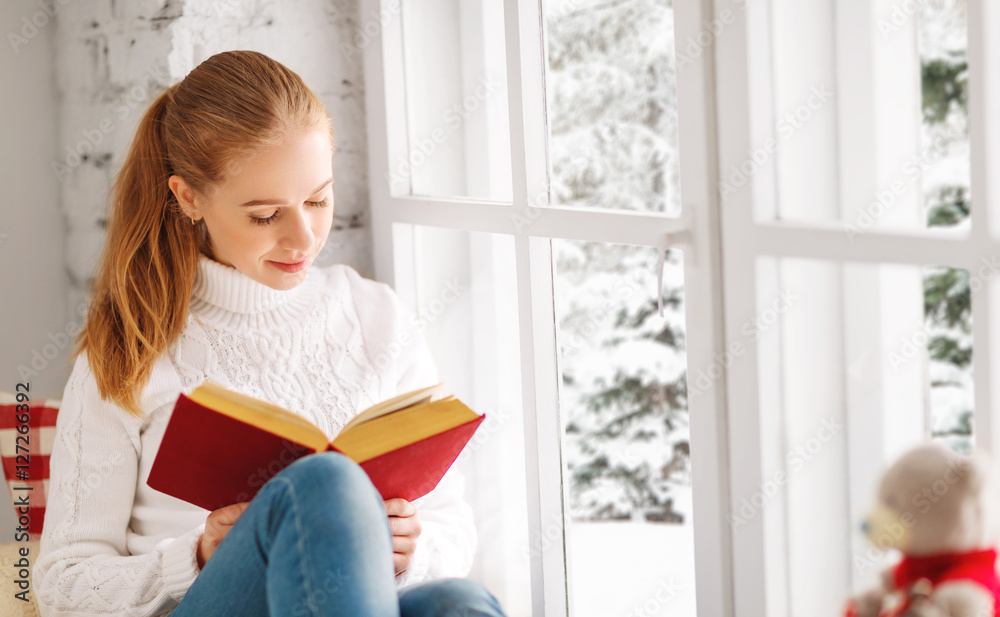 快乐的年轻女人在冬天靠窗看书