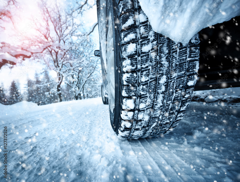 冬季道路上的汽车轮胎被雪覆盖。早上下雪时，车辆在雪地小巷上行驶