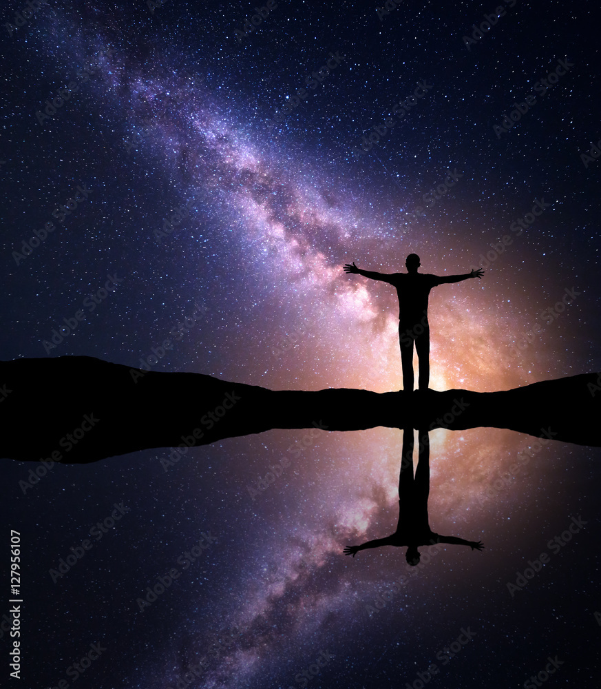 银河系。夜晚星光灿烂，一个独自站立的人的侧影，举起双臂站在山上