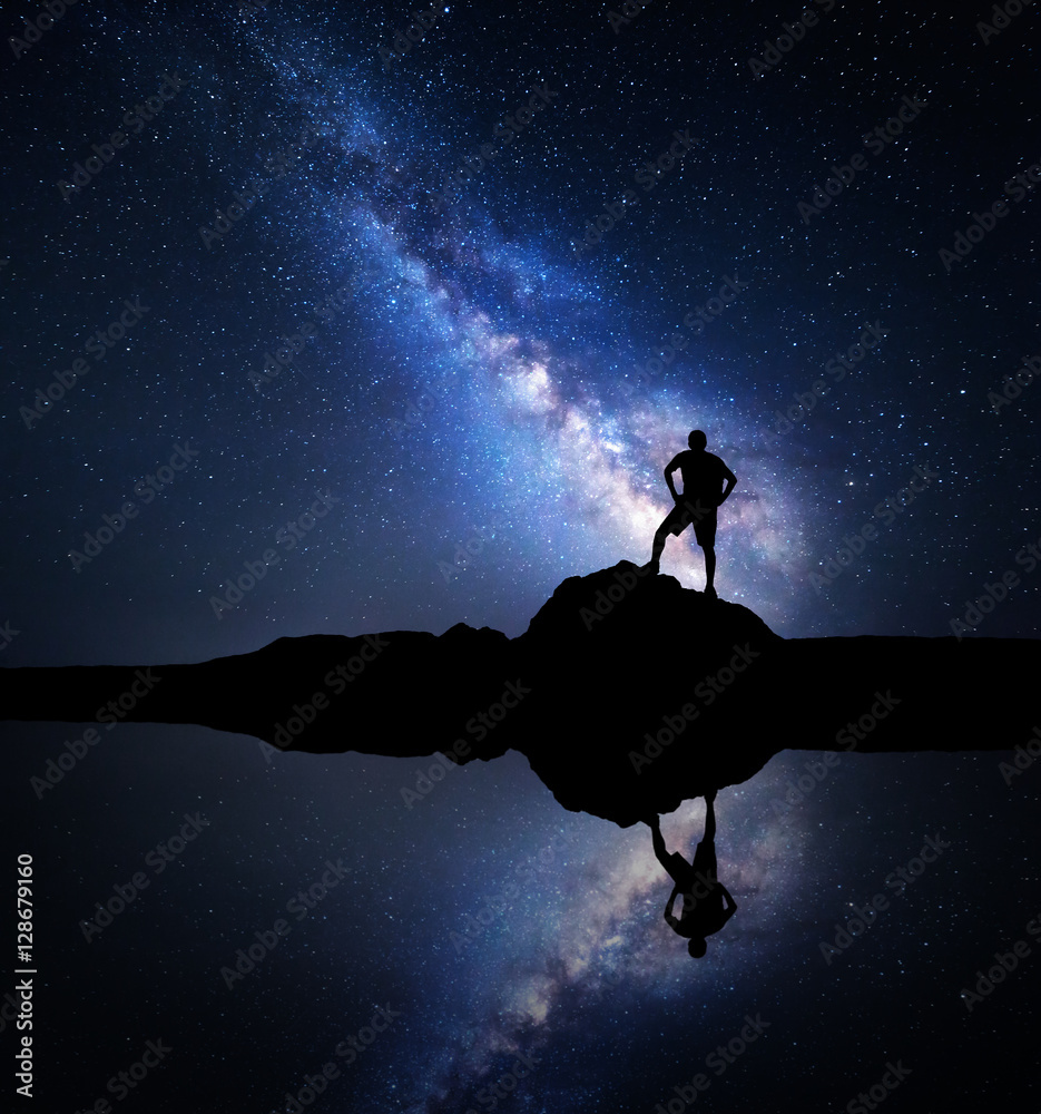 银河系。夜晚的星空和一个背着背包站在lak附近石头上的男人的剪影