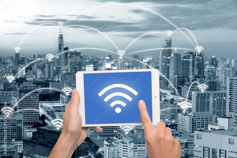 Hand holding tablet with wifi icon on city and network connectio