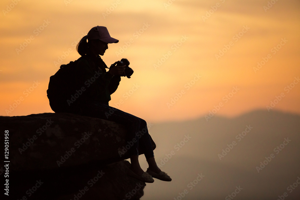 Silhouette girl photographer sitting on the rocks at high shooti