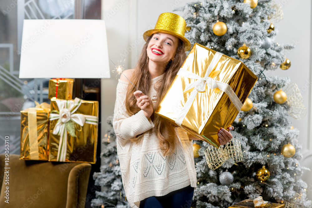 年轻微笑的女人，穿着毛衣，戴着金色帽子，拿着礼盒，和Be一起庆祝寒假