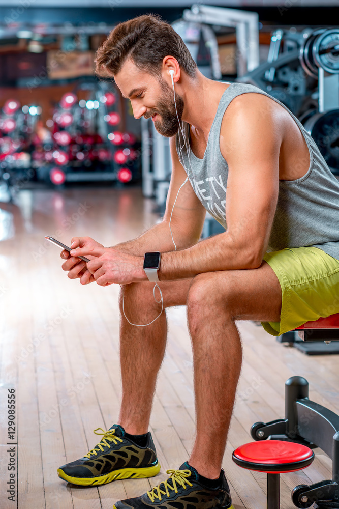 健身房训练结束后，肌肉发达的男子坐在长椅上用手机