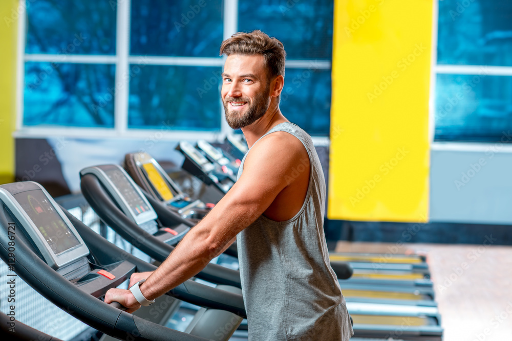 英俊男子在健身房的固定跑步机上进行有氧运动的肖像。