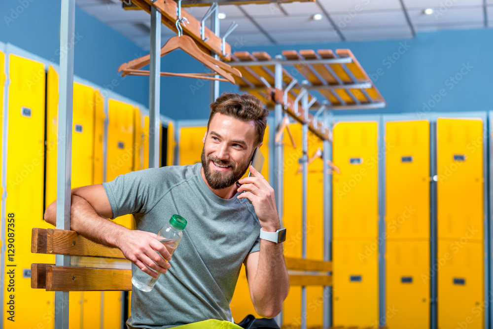 英俊的运动男坐在健身房更衣室里打电话
