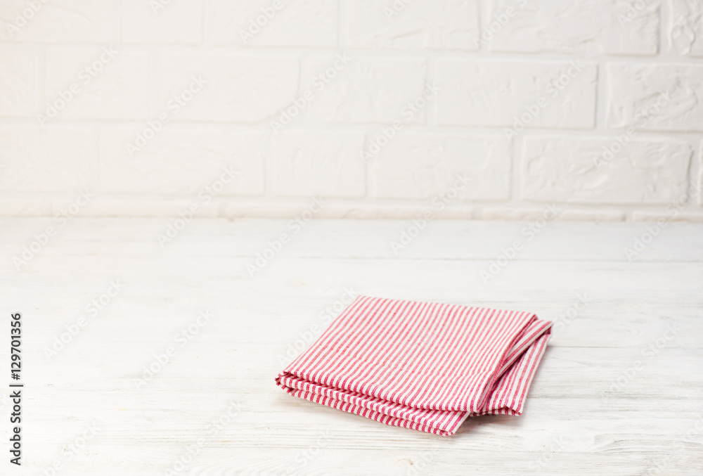 Red napkin isolated on white wooden table. Copy space. Brick wall background. Front view.