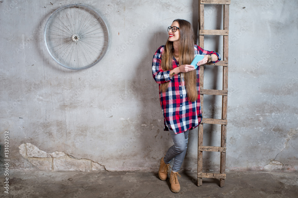 穿着格子衬衫的年轻女子站在旧房间里，灰色纹理的墙上有梯子。