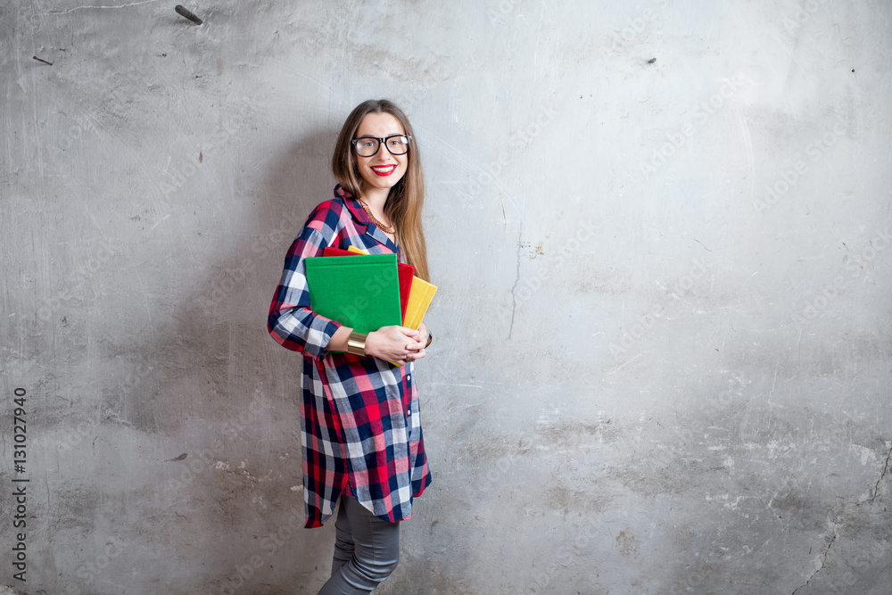 Portrait of a happy young student in checkered shirt with colorful books on the gray wall background