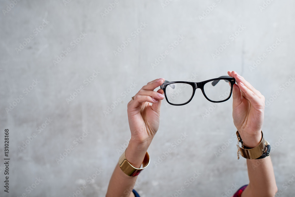 Female hands holding eyeglasses on the gray wall background