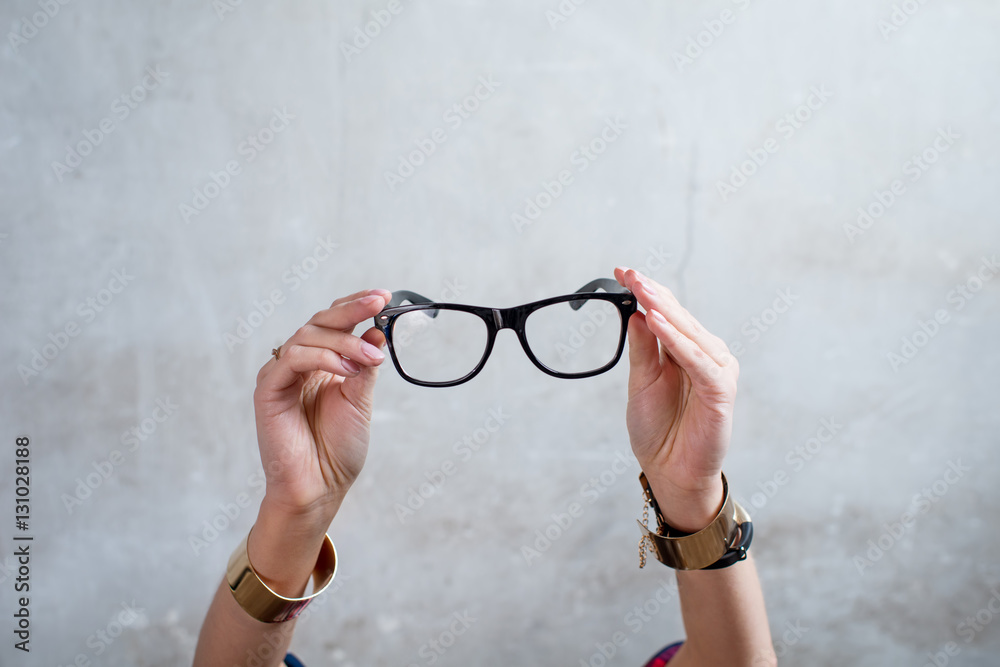 Female hands holding eyeglasses on the gray wall background
