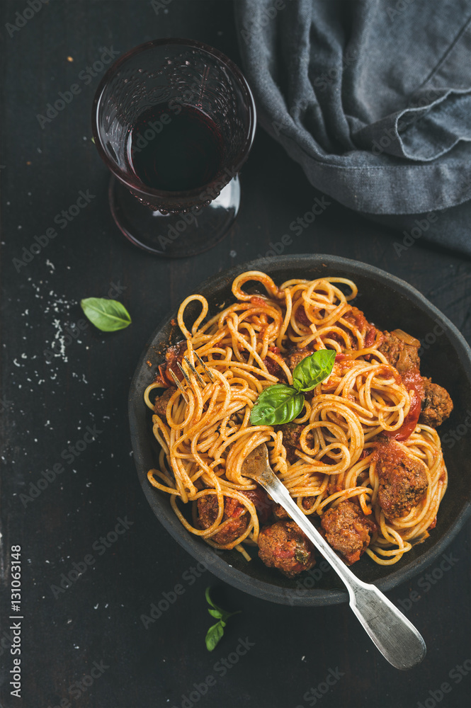 Italian pasta dinner. Spaghetti with meatballas, fresh basil leaves in dark plate and red wine in vi